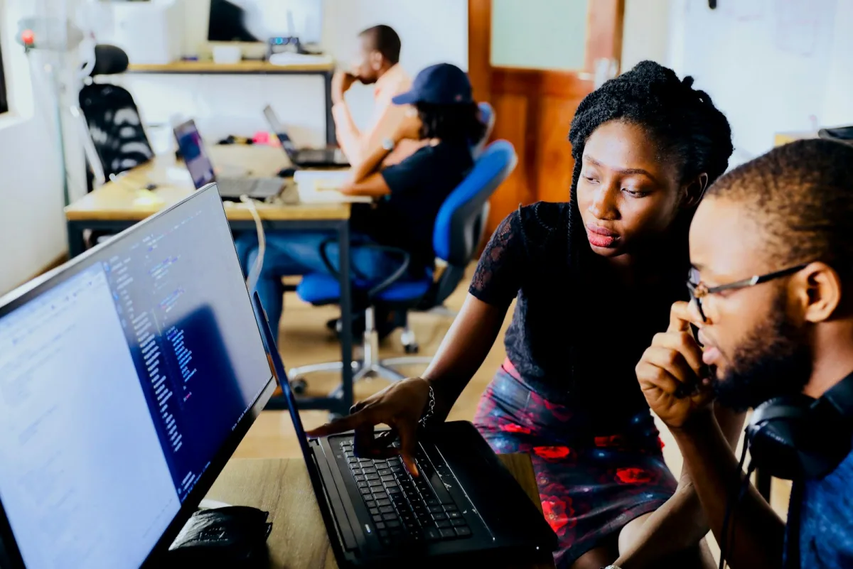 Two colleagues reviewing code together on a laptop in an office